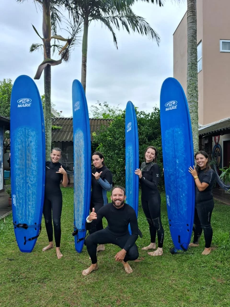 Grupo de cinco pessoas com trajes de surf na areia do Campeche